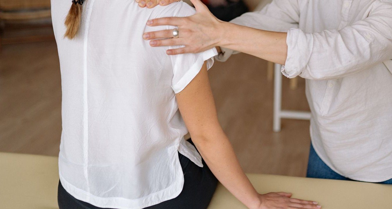 Fisioterapeuta trabajando los hombros y el trapecio de una paciente sentada.